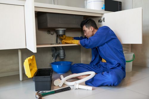 Young Vietnamese plumber checking drain in kitchen