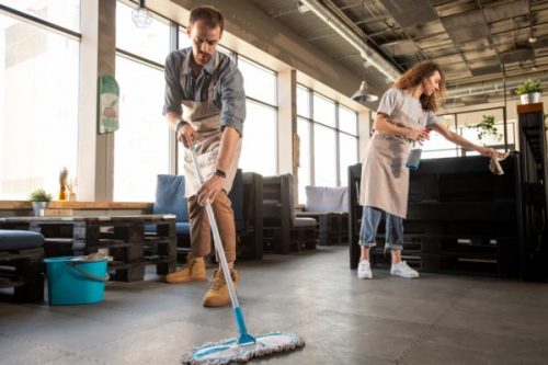 Busy young couple in aprons doing cleaning in cafe while preparing it for opening, small business concept