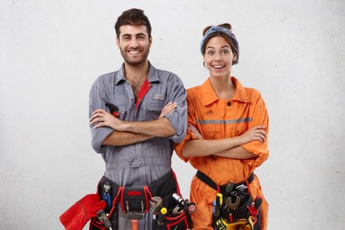 Content female and male technicians in special uniform keep hands folded as wait for instruction from work superintendent or foreman, have smiles as being yet not tired, full of energy and strength