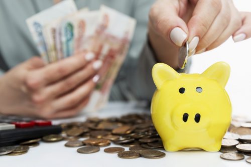 The woman puts coins in a piggy bank. Economical budget allocati